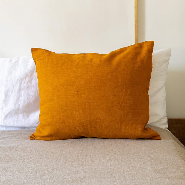 An amber yellow linen throw pillow with zipper on a bed, with a white wall in the background. Mix and match the colours of the throw pillows and create a unique atmosphere at home.