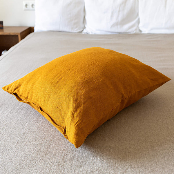 An amber yellow linen throw pillow with zipper on a bed, with a white wall in the background. Mix and match the colours of the throw pillows and create a unique atmosphere at home.