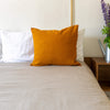 An amber yellow linen throw pillow with zipper on a bed, with a white wall in the background. Mix and match the colours of the throw pillows and create a unique atmosphere at home.