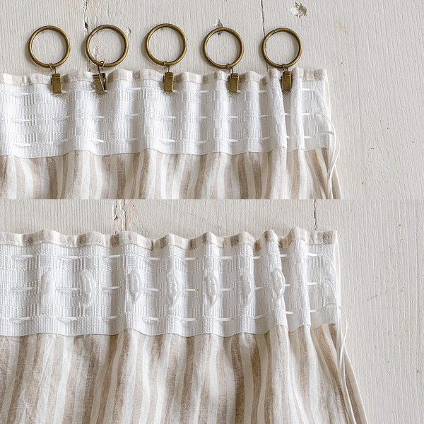 White textured curtain with gold rings and clips on a light wooden background