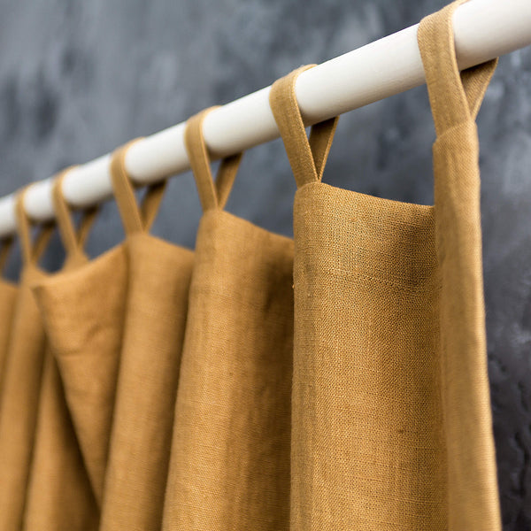 Dusty Mustard aprons hanging on a white rod against a dark background