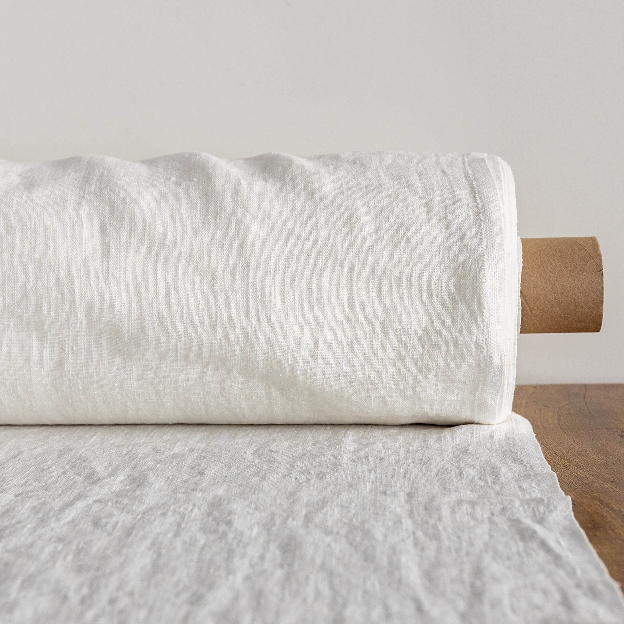 Rolled-up antique white fabric on a wooden surface with a neutral background