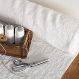 Spools of white thread in a wooden box with scissors on a antique white fabric-covered surface