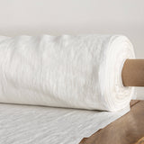Roll of antique white fabric on a wooden surface with a neutral background