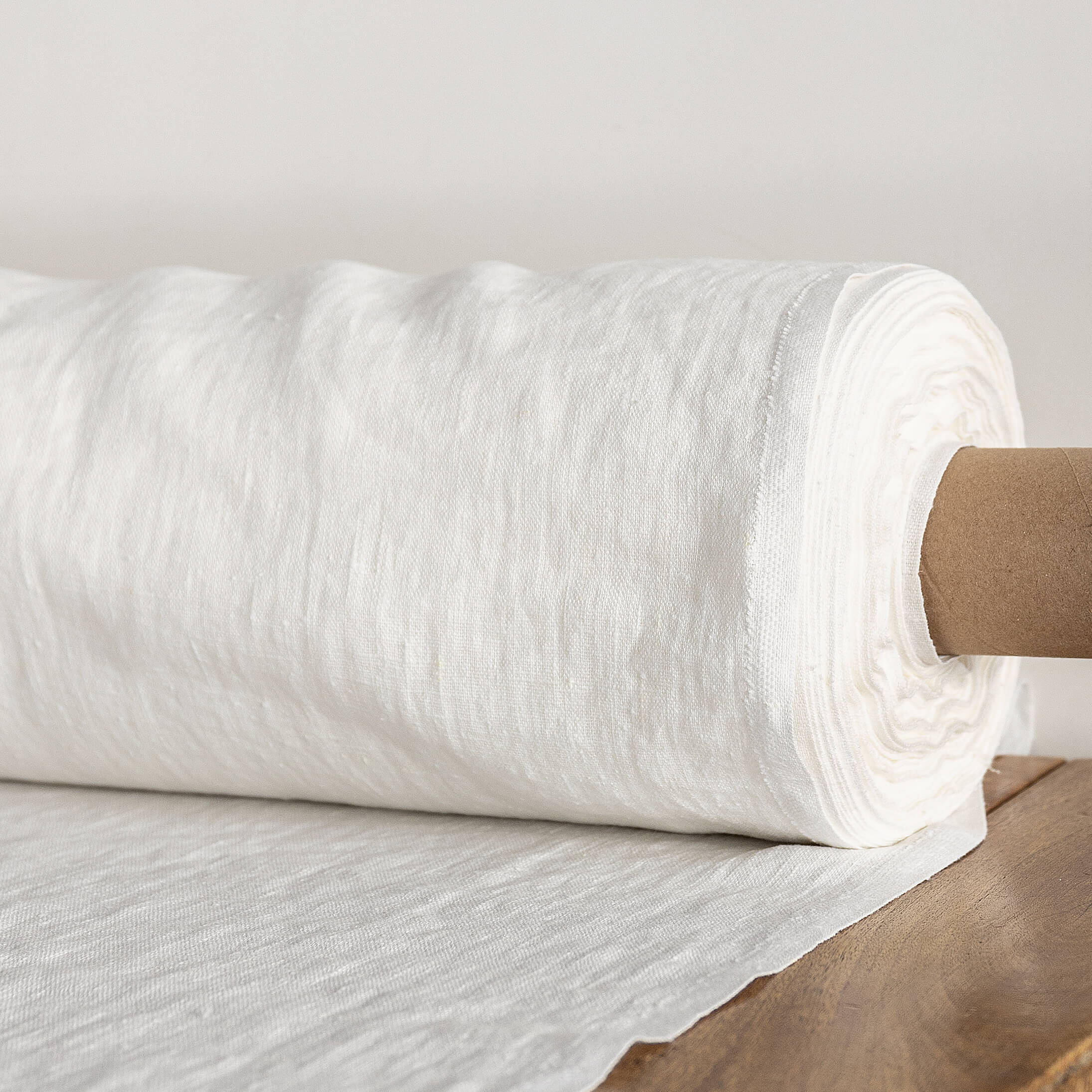 Roll of antique white fabric on a wooden surface with a neutral background