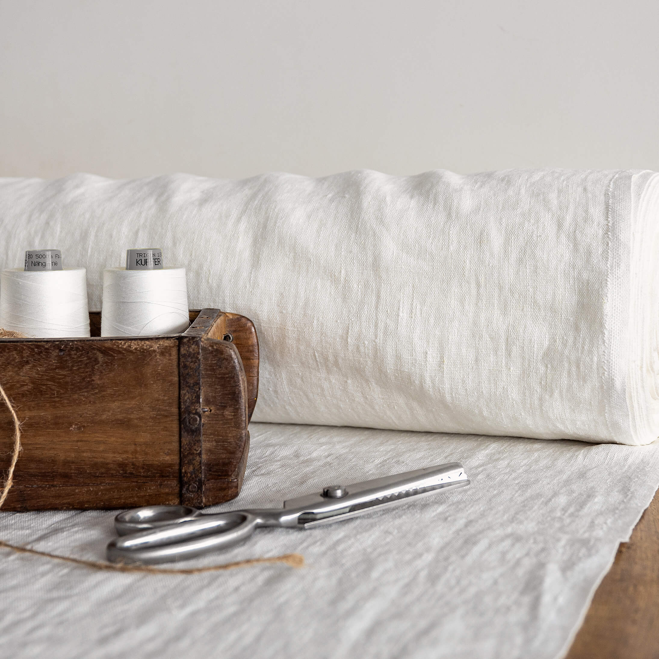 Wooden box with spools of white thread and a pair of scissors on a fabric-covered surface.