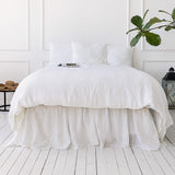 Bri
ght White bed with a white comforter in a minimalistic room with a plant and side table.