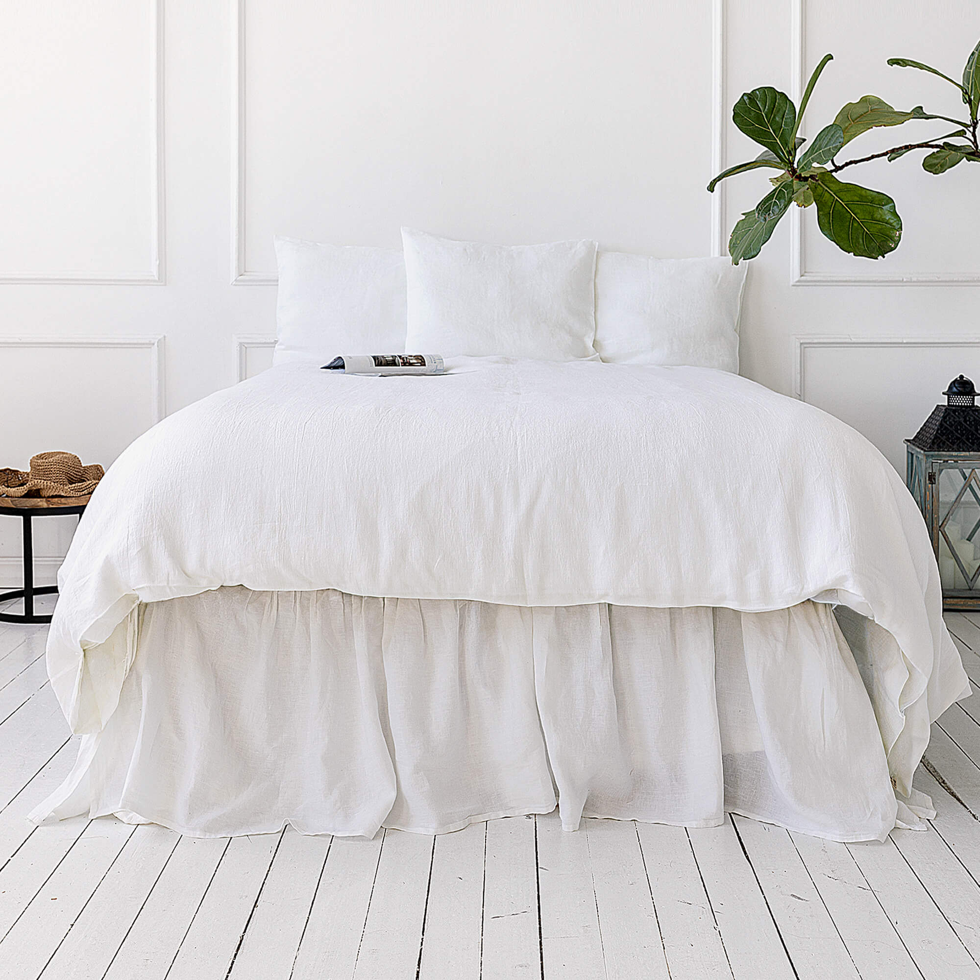 Bri
ght White bed with a white comforter in a minimalistic room with a plant and side table.