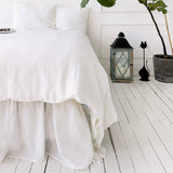 Bright White bed with a white duvet on a white wooden floor, with a lantern and plant in the background.