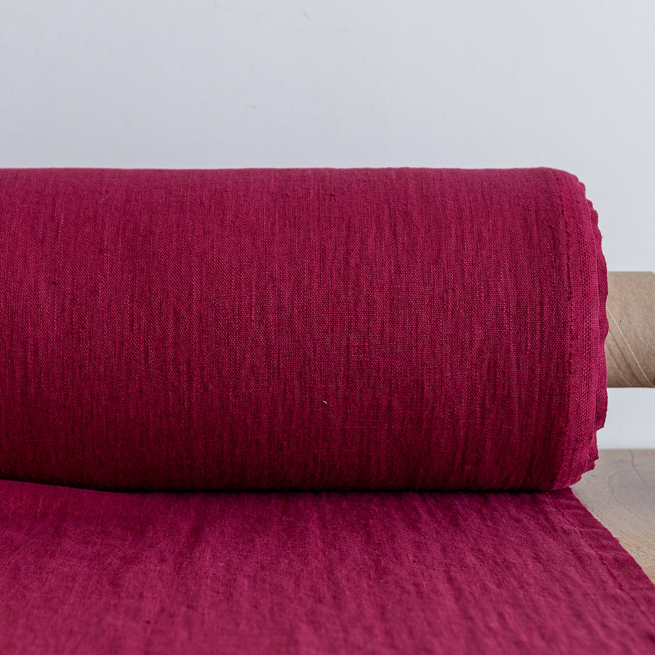 Roll of burgundy red fabric on a light gray background