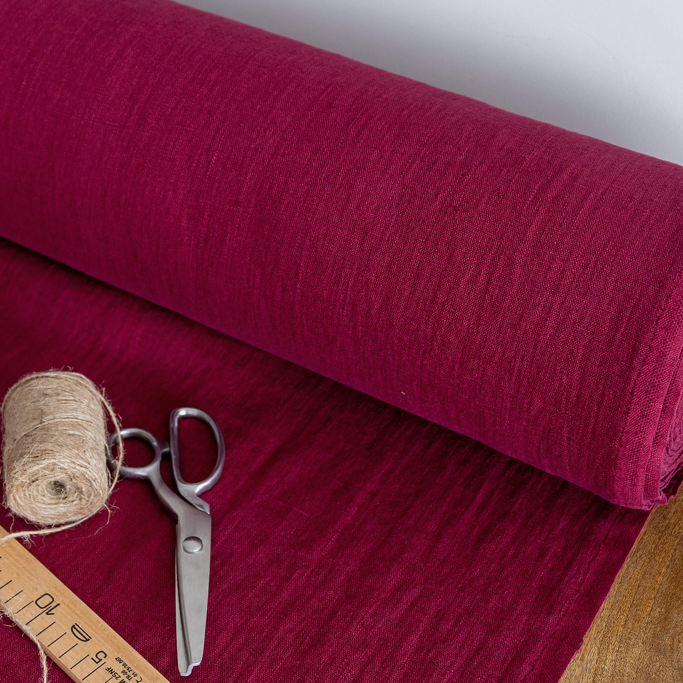 Roll of burgundy red fabric with scissors and thread on a matching background