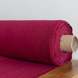 Roll of burgundy red fabric on a wooden surface with a white background