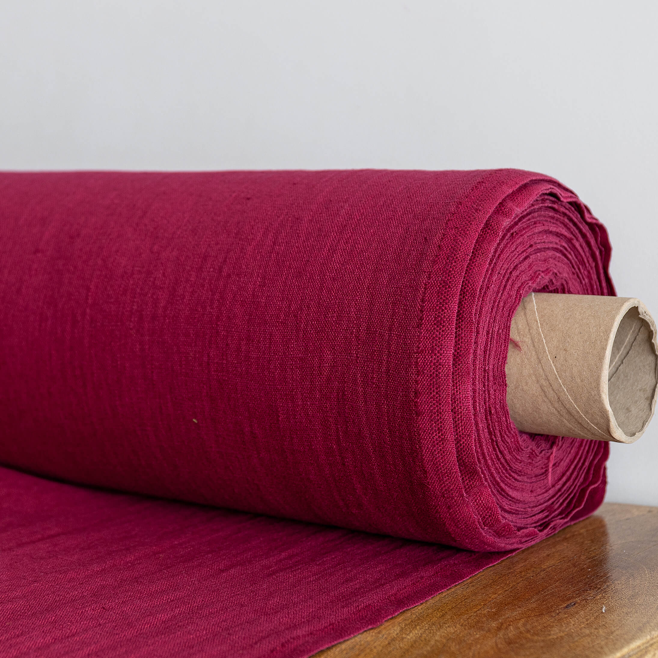 Roll of burgundy red fabric on a wooden surface with a white background