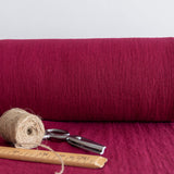Roll of burgundy red fabric with scissors and twine on a matching background