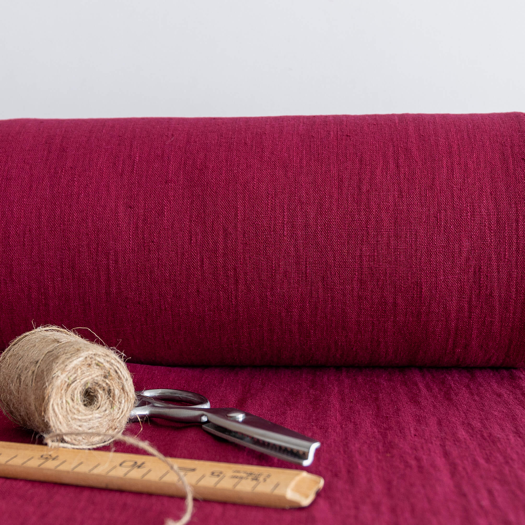 Roll of burgundy red fabric with scissors and twine on a matching background
