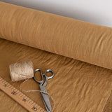 Roll of dusty mustard fabric with scissors, thread, and a ruler on a wooden surface.