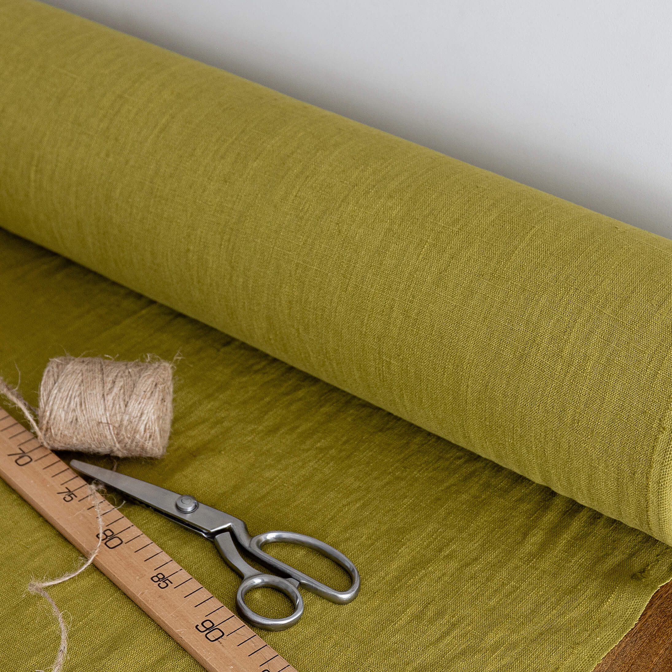 Roll of olive green fabric with scissors, thread, and a ruler on a white background