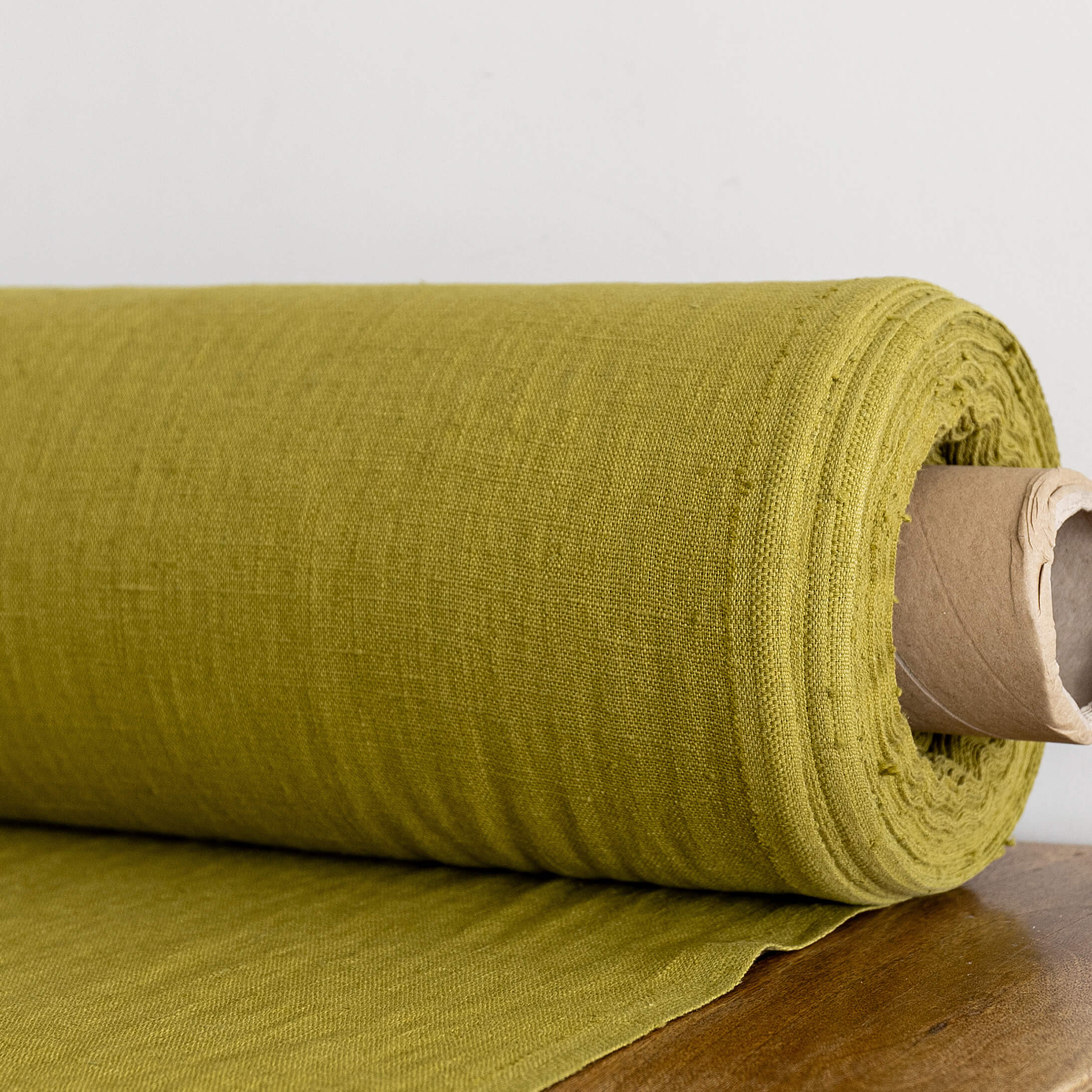 Rolled-up olive green fabric on a wooden surface with a neutral background