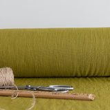 Roll of olive green fabric with scissors and thread on a matching background
