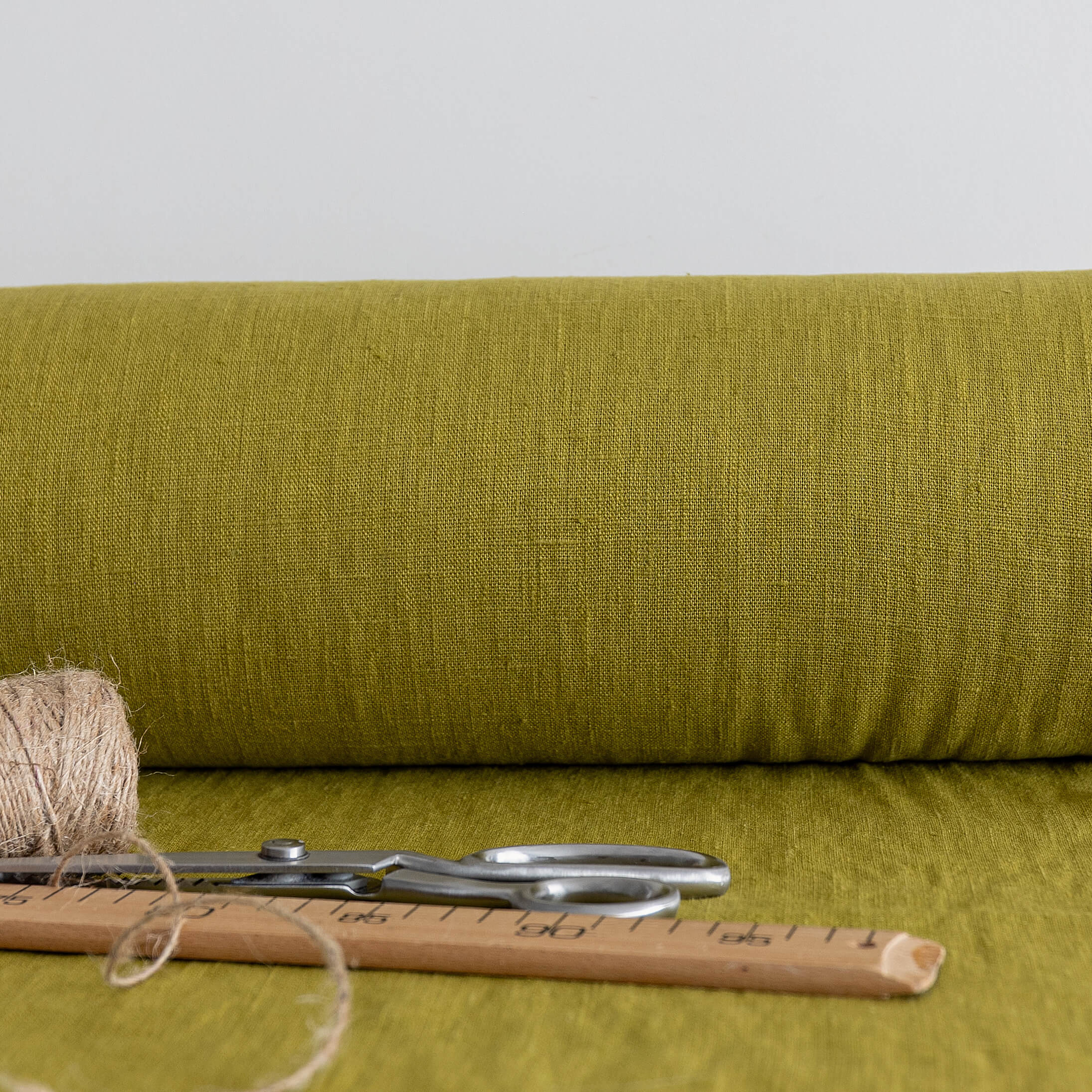 Roll of olive green fabric with scissors and thread on a matching background