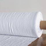 Roll of optical white textured fabric on a wooden surface with a neutral background