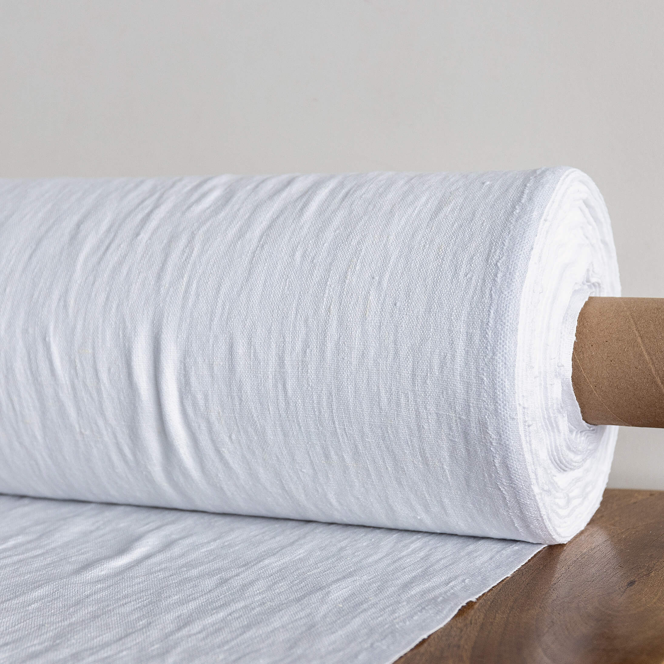 Roll of optical white textured fabric on a wooden surface with a neutral background