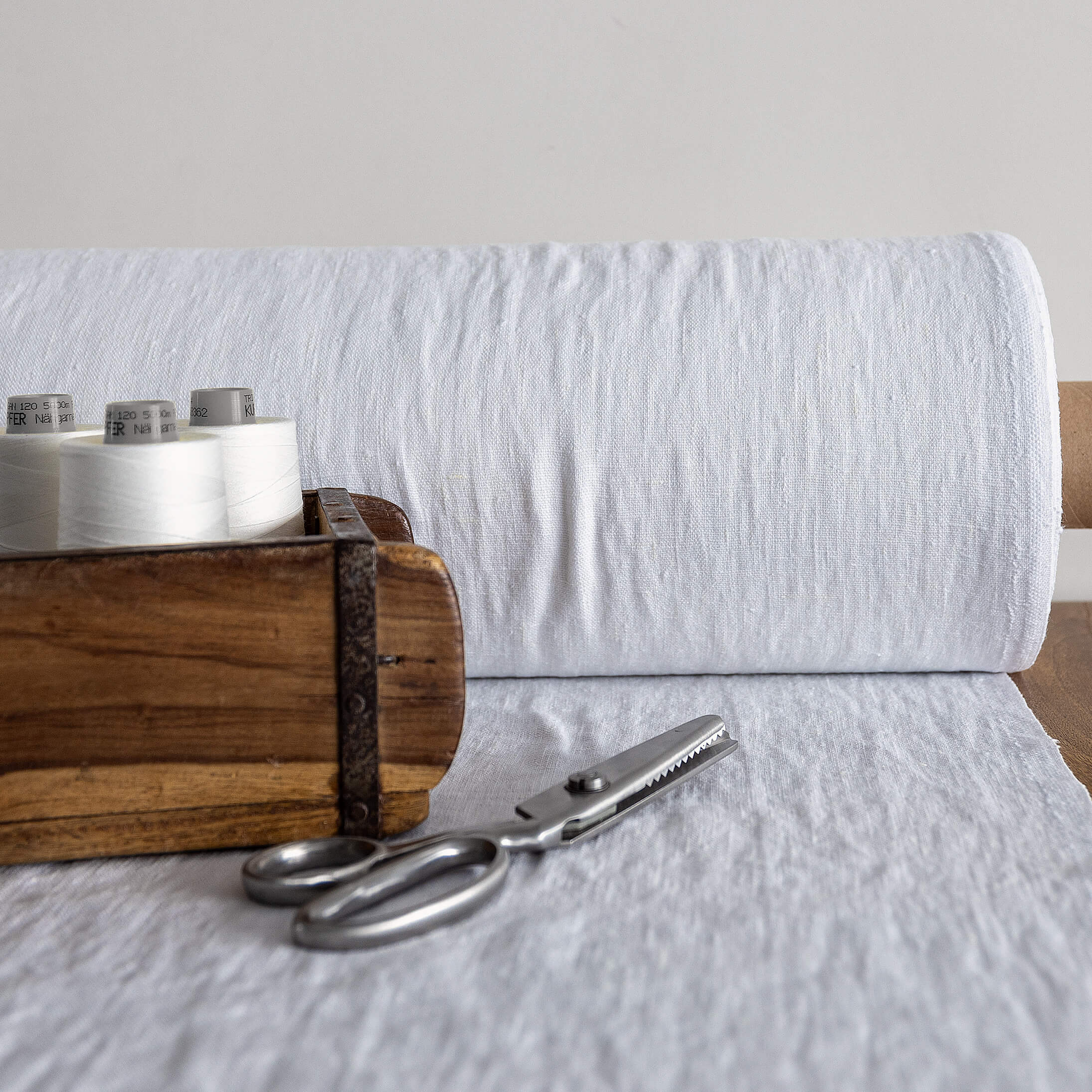Wooden box with spools of thread and a pair of scissors on a optical white fabric background