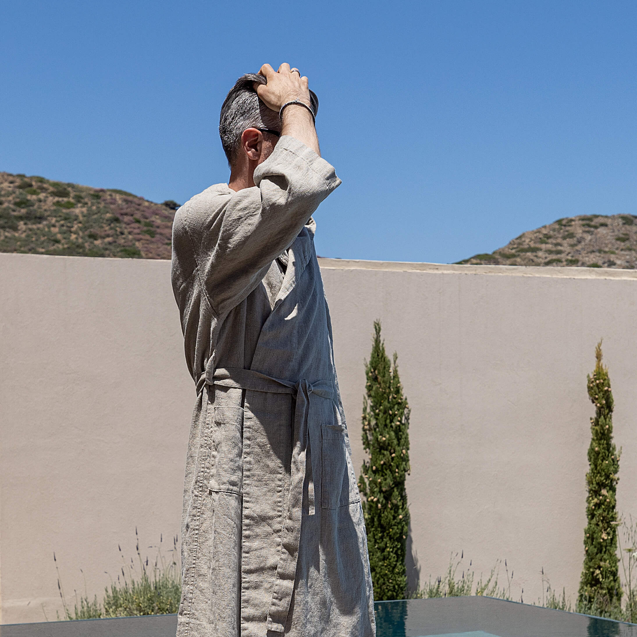 Man in a natural linen batrobe standing outdoors with mountains in the background