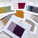 Collection of fabric swatches from The Linen Valley on a light wooden surface.