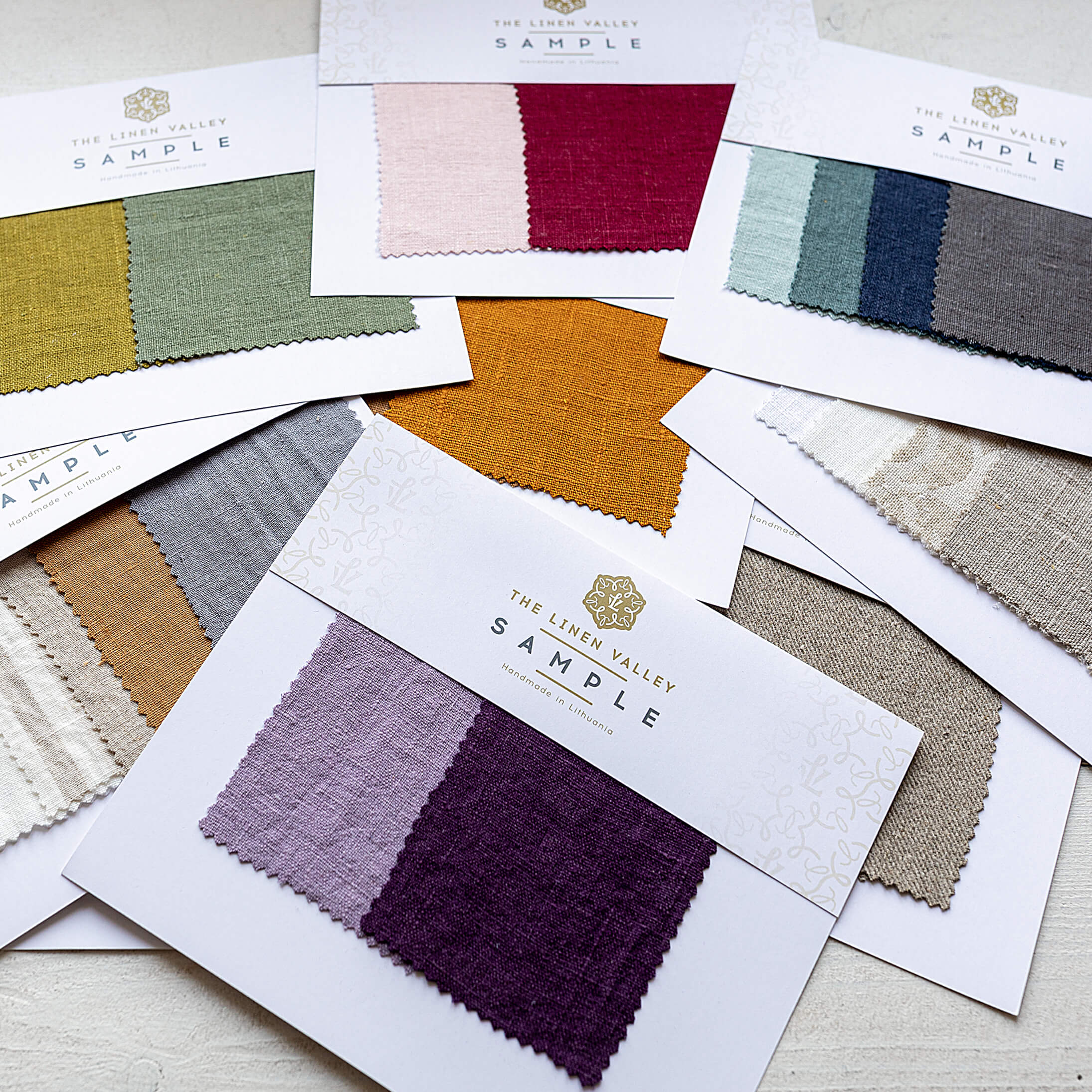 Collection of fabric swatches from The Linen Valley on a light wooden surface.