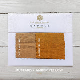 Linen Valley fabric sample card with mustard and amber yellow swatches on a wooden surface.