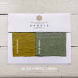 Fabric sample card with olive and moss green swatches on a wooden surface.