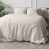 Beige textured duvet cover set on a bed in a bedroom with plants and a chair.