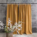 Dusty Mustard curtains hanging against a gray wall with white floral branches in a vase.