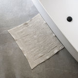 Beige textured towel on a gray tiled floor next to a white sink.