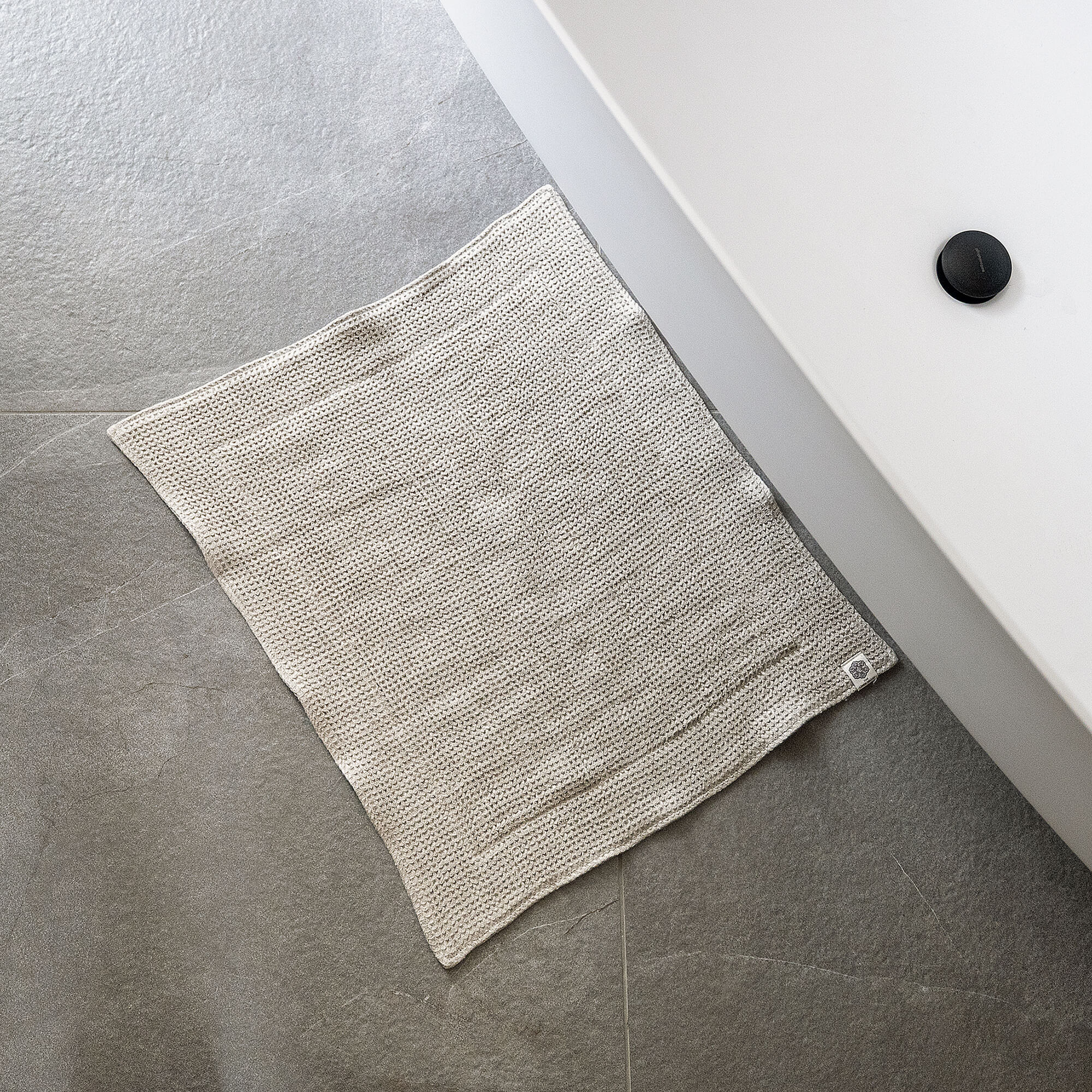 Beige textured towel on a gray tiled floor next to a white sink.