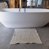 White freestanding bathtub in a bathroom with a textured rug on the floor.