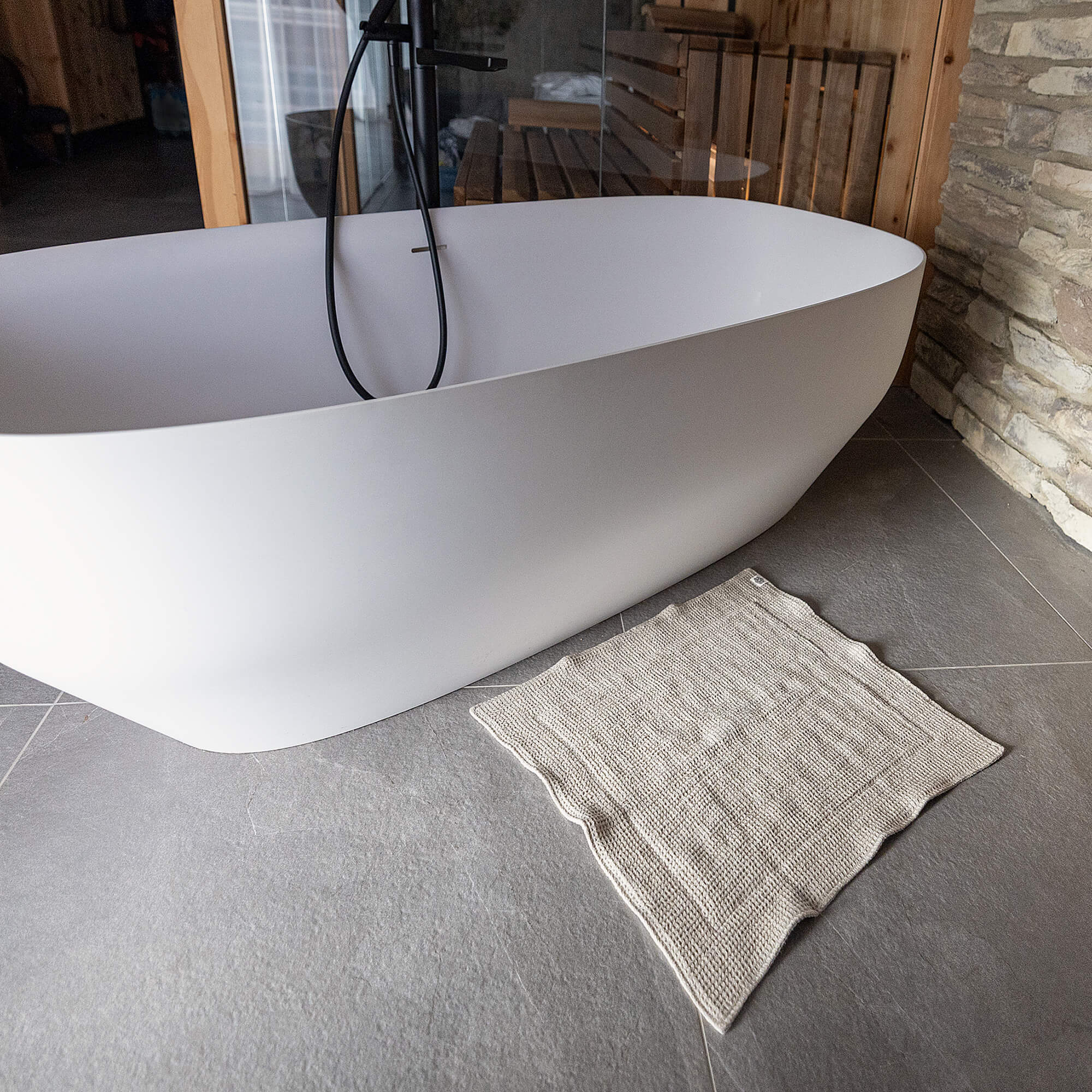 White freestanding bathtub in a modern bathroom with a textured rug on the floor.