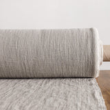 Roll of unbleached linen fabric on a wooden surface with a light grey background
