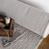 Roll of unbleached linen fabric with a wooden box containing thread and scissors on a wooden surface.