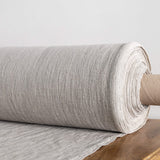 Roll of unbleached linen fabric on a wooden surface with a light grey background