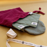 Burgundy linen gift bag with moss green oven mitts inside