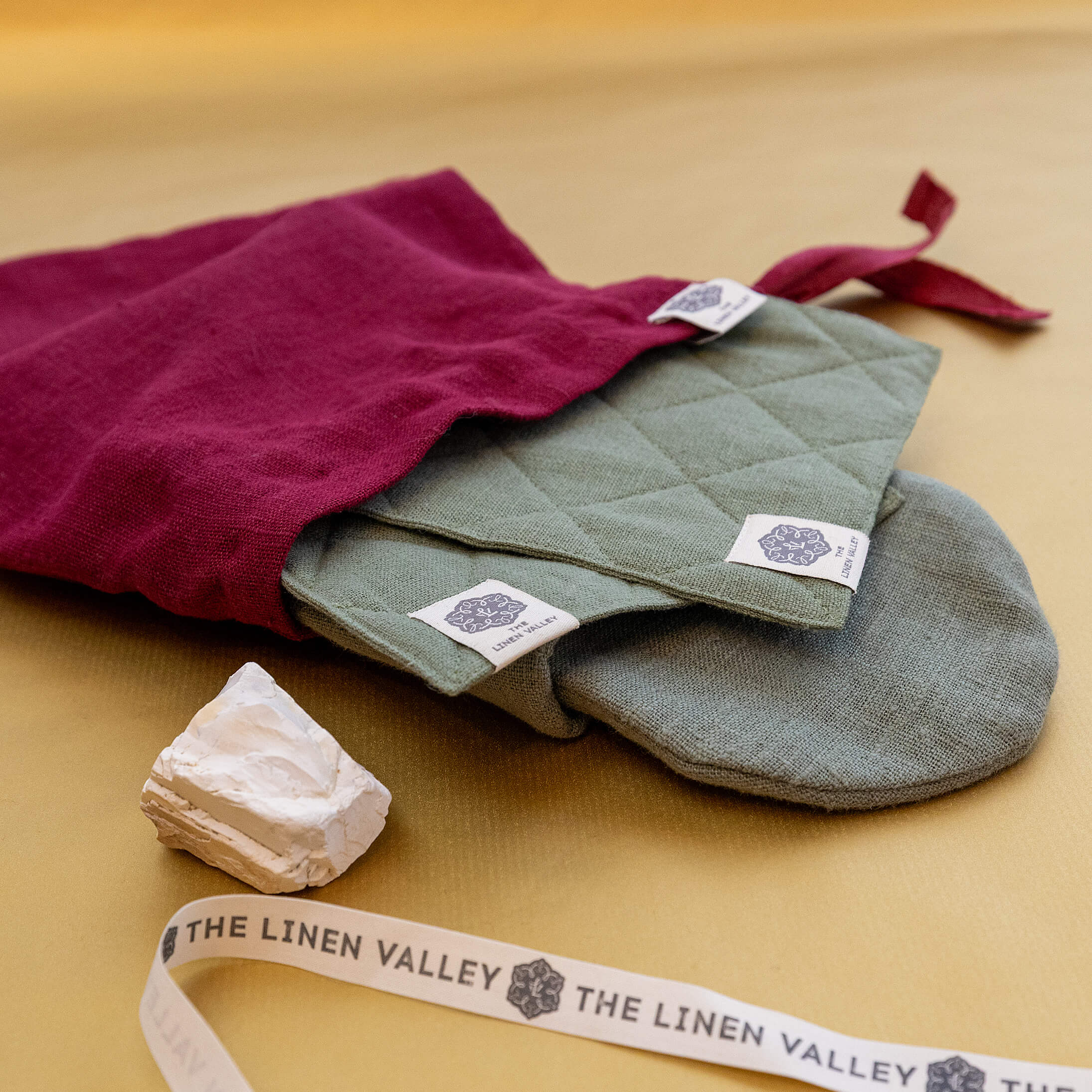 Burgundy linen gift bag with moss green oven mitts inside